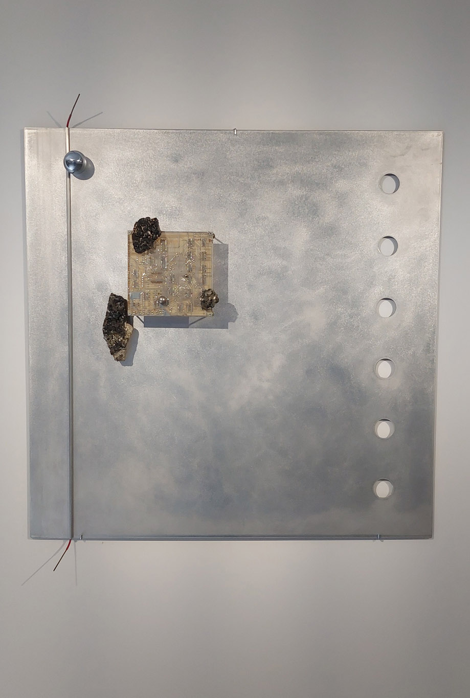 Michel Scheer, Fractal, 2016, sur plaque de métal argenté perforé, une boule argentée sur ligne argentée verticale, un circuit intégré électronique et 3 petits cailloux en lave, exposition En Regard, Le Delta, Namur , 2023, Boombartstic Art Magazine