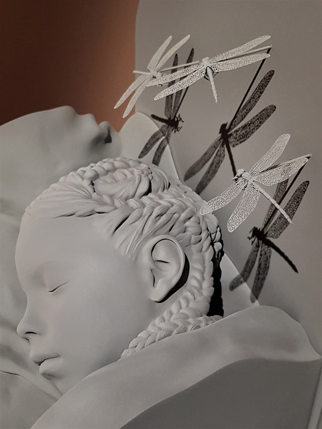 Hans Op de Beeck, Girl Asleep, 2021, visage gris d'une fillette endormie, rêvant, cheveux tressés au-dessus desquels volent trois libellules, exposition Silence & Résonance, Musée de Flandre, Cassel, France, 2023, Boombartstic Art Magazine, Bruxelles