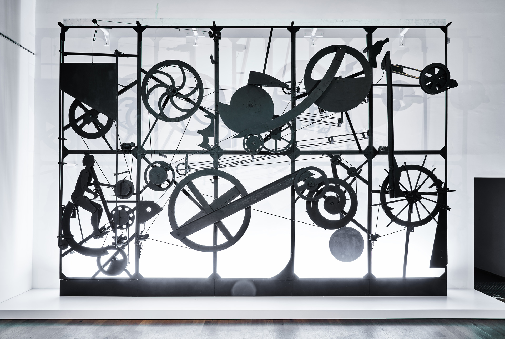 Jean Tinguely, Eloge de la Folie, 1966, cadre en aluminium et roues en bois, câble, courroies en caoutchouc, moteurs électriques, le tout peint en noir, 540 x 780 x 75 cm, vue de l'installation au Musée Tinguely, Bâle, Suisse, Année Jean Tinguely 100 - Centenaire, (c) 2024 ProLitteris, Zürich, (c) photo Museum Tinguely, Bâle, photo Daniel Spehr, Boombartstic Art Magazine