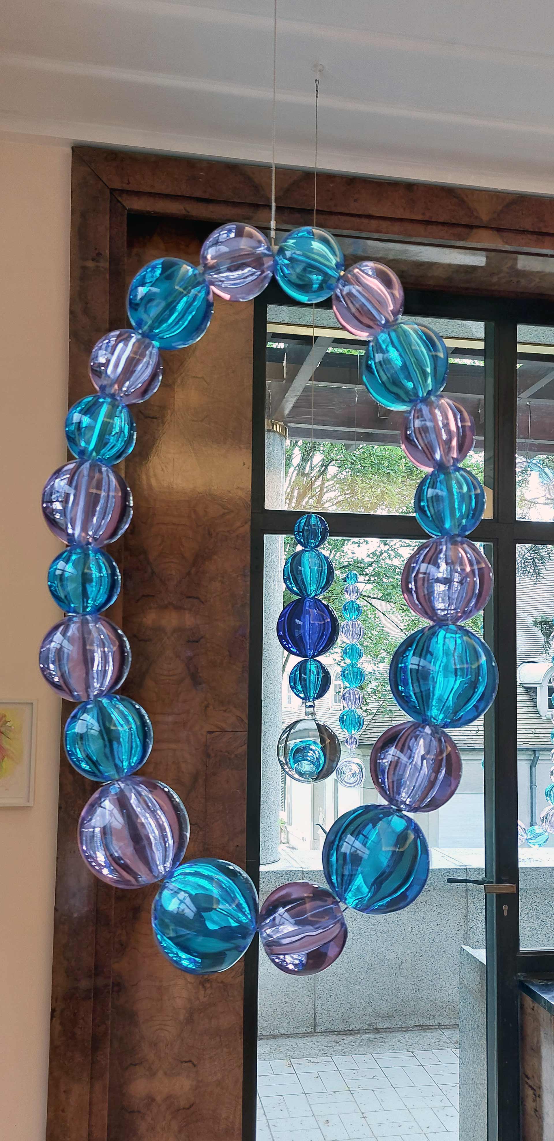 Jean-Michel Othoniel, Colliers et amants suspendus , 2017, Verre de Murano alessandrita et aquamarine, inox et Verre de Murano aquamarine et cristal, inox, exposition Diary of Happiness, Fondation Boghossian - Villa Empain, 2026, (c) Othoniel Studio_Jean-Philippe Robin, (c) photo Eric Mabille - Boombartstic Art Magazine